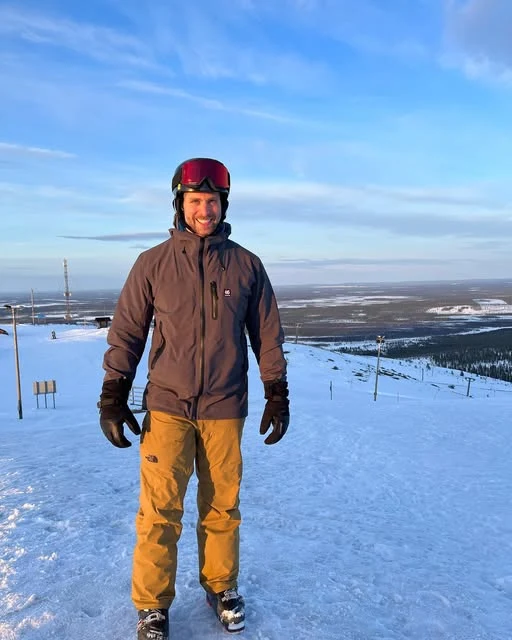 Brad Dworkin in a helmet, winter jacket and yellow snow pants on a snowy mountain.
